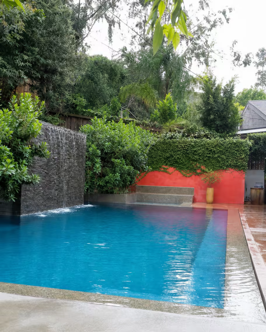 Pool with a stone waterfall wall in a lush garden